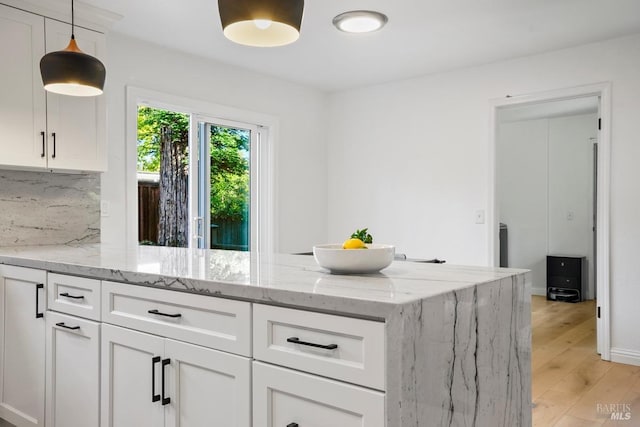 kitchen with light wood-style flooring, light stone counters, white cabinetry, a peninsula, and tasteful backsplash