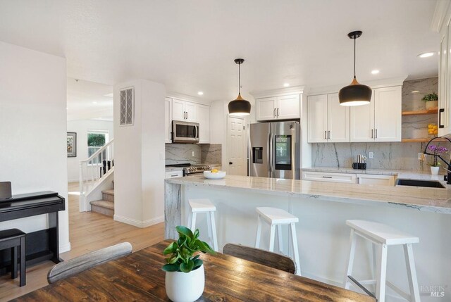kitchen featuring a peninsula, appliances with stainless steel finishes, light stone counters, a breakfast bar area, and light wood-style floors