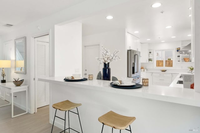 kitchen featuring high quality fridge, wall chimney exhaust hood, a kitchen bar, a peninsula, and recessed lighting