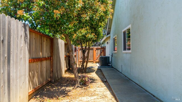 view of side of home with a fenced backyard, stucco siding, and central AC unit