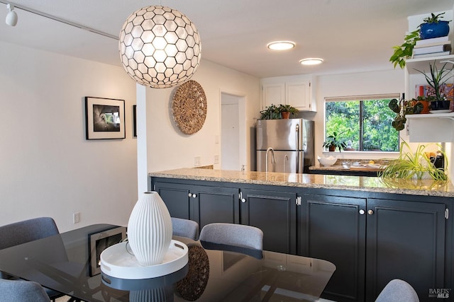 kitchen featuring freestanding refrigerator, light stone counters, white cabinets, and a peninsula