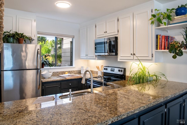 kitchen with appliances with stainless steel finishes, white cabinetry, dark stone countertops, and a sink