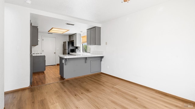 kitchen with freestanding refrigerator, gray cabinetry, tile countertops, a kitchen breakfast bar, and a peninsula