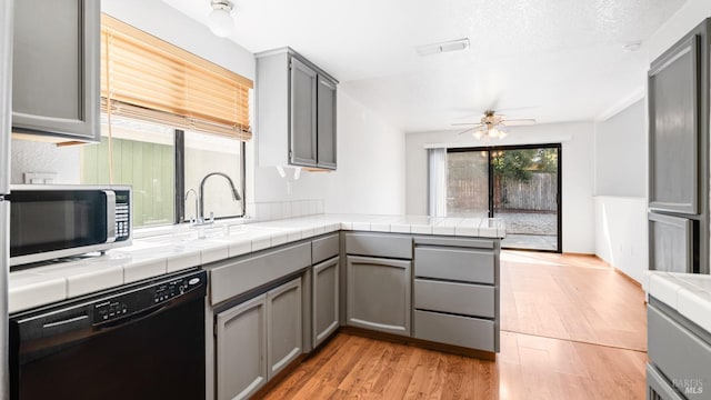 kitchen with black dishwasher, stainless steel microwave, gray cabinets, a sink, and ceiling fan