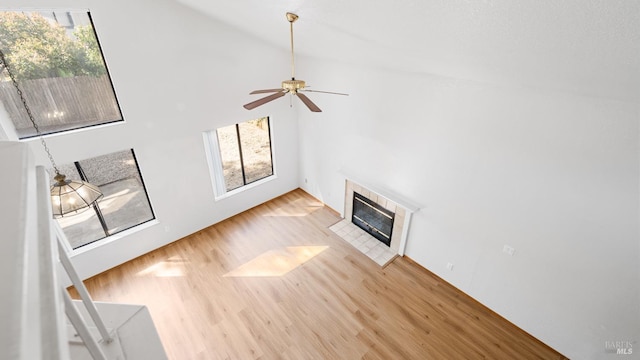 unfurnished living room with wood finished floors, a tile fireplace, high vaulted ceiling, healthy amount of natural light, and a ceiling fan