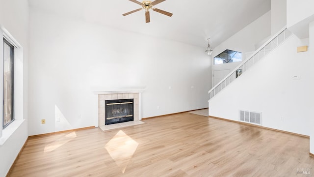 unfurnished living room featuring a towering ceiling, stairway, a ceiling fan, wood finished floors, and a tile fireplace