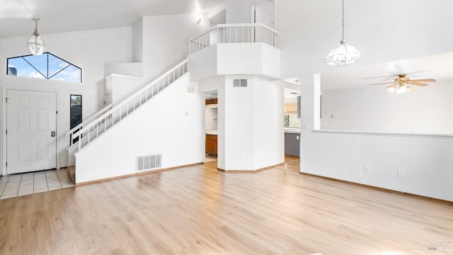 foyer with a chandelier, a towering ceiling, light wood-style flooring, stairs, and a ceiling fan