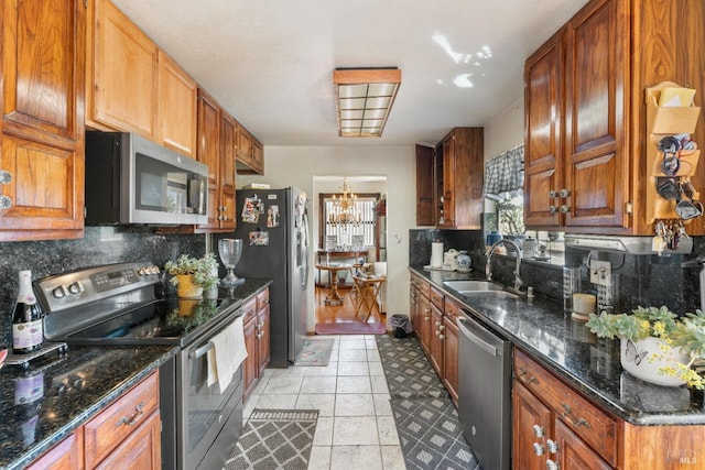 kitchen with appliances with stainless steel finishes, a sink, backsplash, brown cabinets, and a chandelier