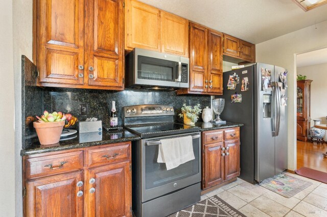 kitchen featuring stainless steel appliances, decorative backsplash, brown cabinets, and dark stone countertops