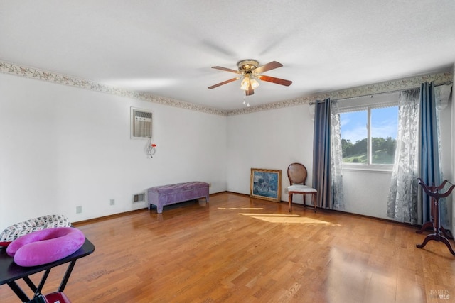 sitting room with ceiling fan, light wood-type flooring, baseboards, and a wall mounted AC