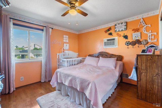 bedroom featuring wood finished floors, a wall mounted air conditioner, baseboards, and ceiling fan