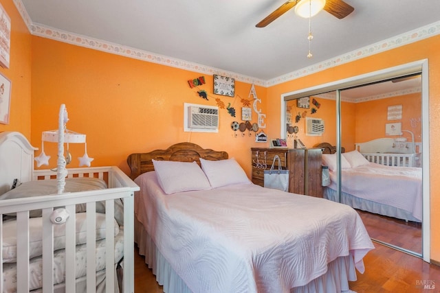 bedroom with an AC wall unit, wood finished floors, a closet, ornamental molding, and ceiling fan