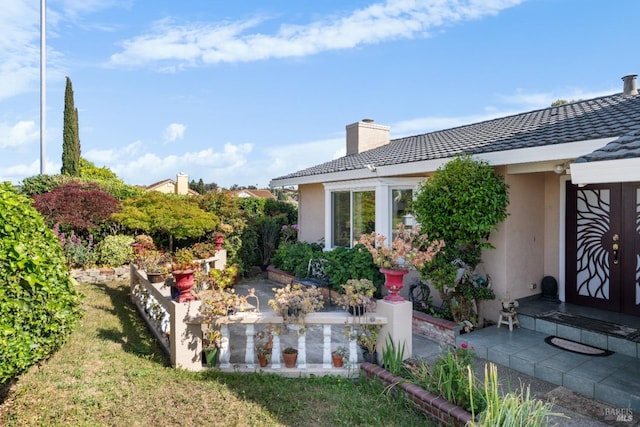 rear view of property with stucco siding, a chimney, a tile roof, and a patio area