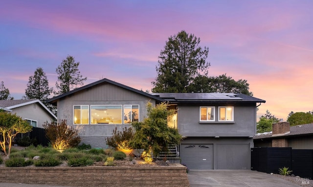 view of front facade featuring roof mounted solar panels, driveway, fence, an attached garage, and stucco siding