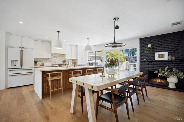 dining area with light wood finished floors, recessed lighting, and a brick fireplace