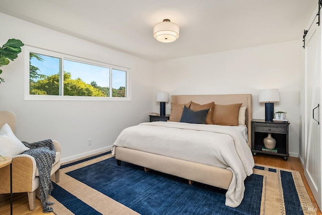 bedroom with a barn door, baseboards, and wood finished floors