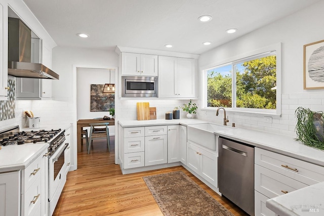 kitchen with appliances with stainless steel finishes, wall chimney range hood, tasteful backsplash, a sink, and recessed lighting