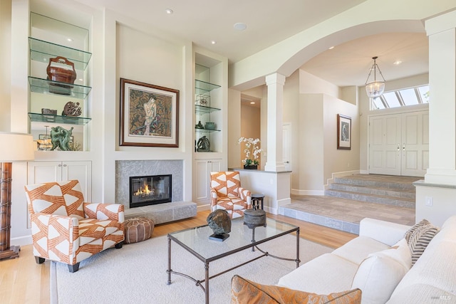 living area featuring decorative columns, wood finished floors, built in shelves, a fireplace, and recessed lighting