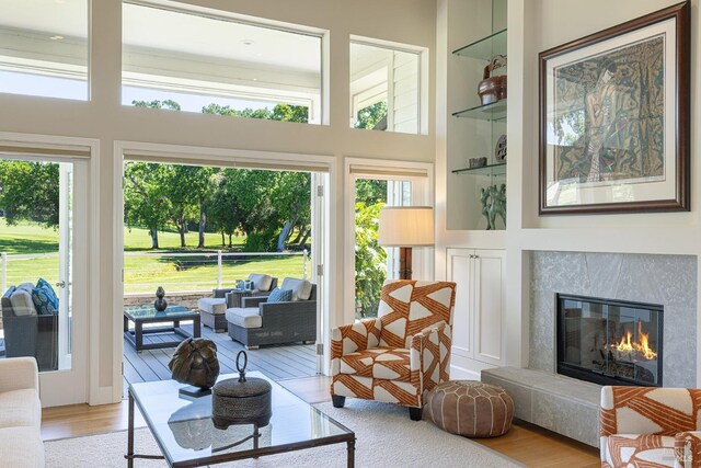 living area featuring light wood-style flooring, a premium fireplace, built in shelves, and a high ceiling