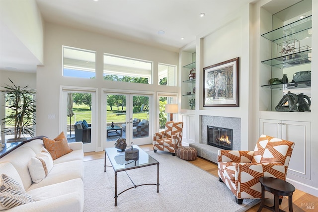 living area featuring light wood-type flooring, built in features, a premium fireplace, french doors, and recessed lighting