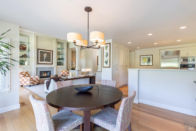 dining space with light wood finished floors, a chandelier, a glass covered fireplace, baseboards, and recessed lighting