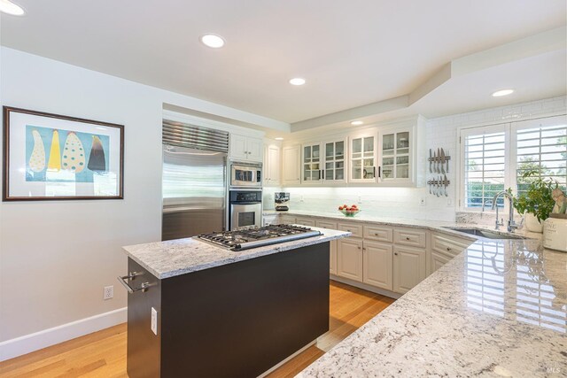 kitchen featuring a sink, built in appliances, light stone countertops, decorative backsplash, and light wood finished floors