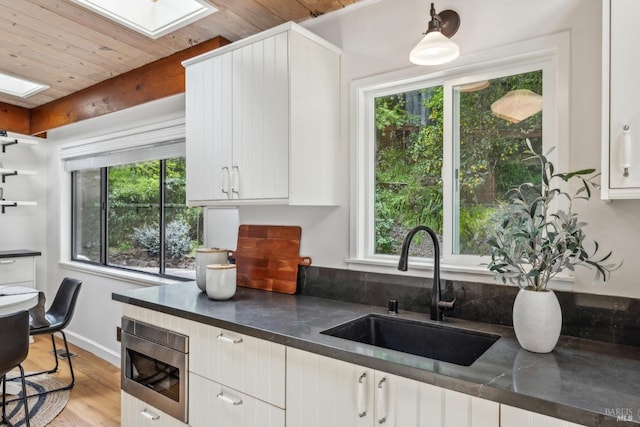 16 Ivy Ln, Woodacre, CA 94973 - kitchen featuring a skylight, a sink, dark countertops, light wood finished floors, and white cabinetry