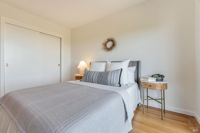 bedroom with wood finished floors, baseboards, and a closet