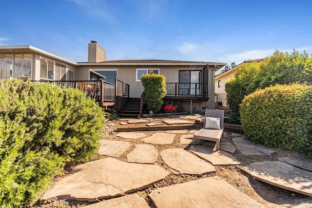 back of property with a wooden deck, a chimney, stairs, stucco siding, and a patio