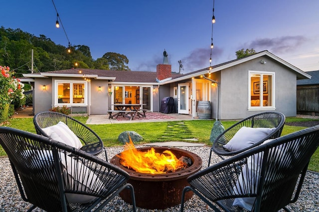 229 Cardinal Rd, Mill Valley, CA 94941 - back of property at dusk with an outdoor fire pit, a patio area, stucco siding, a chimney, and a yard