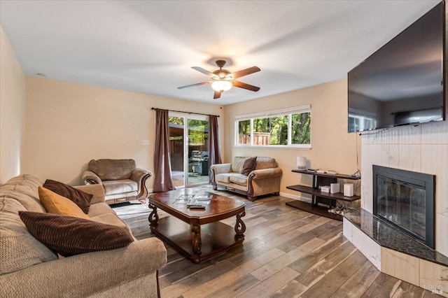 living area with a tile fireplace, a ceiling fan, and wood finished floors