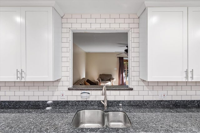 kitchen view of a sink, dark stone countertops, and white cabinetry