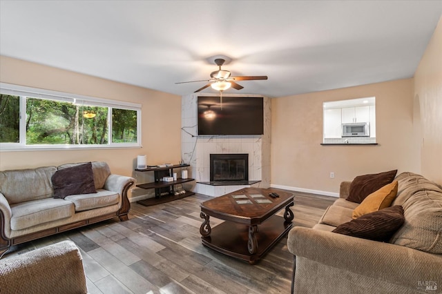 living room featuring a ceiling fan, a tile fireplace, wood finished floors, and baseboards