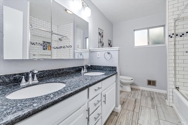 bathroom featuring toilet, double vanity, baseboards, and tiled shower / bath