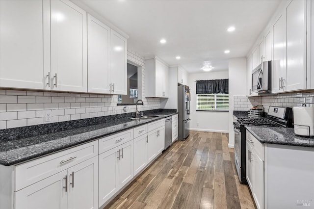 kitchen featuring appliances with stainless steel finishes, a sink, light wood-style floors, white cabinetry, and baseboards