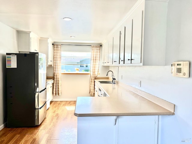 kitchen featuring freestanding refrigerator, a sink, light wood-type flooring, and a peninsula