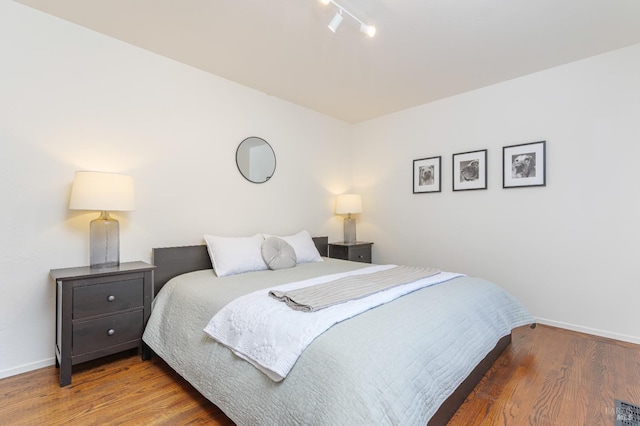 bedroom with baseboards, wood finished floors, and track lighting