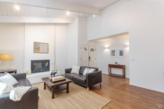 living area with rail lighting, wood finished floors, a brick fireplace, baseboards, and beam ceiling