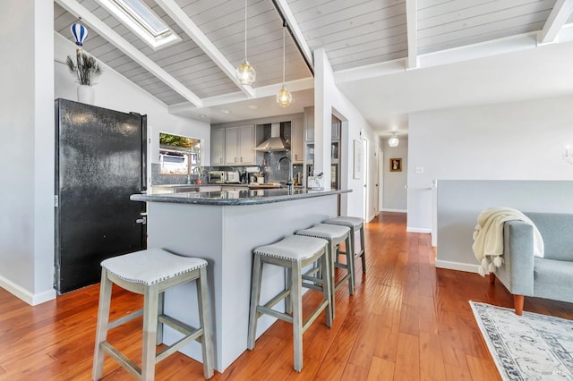 kitchen with wall chimney range hood, a skylight, a breakfast bar area, a peninsula, and freestanding refrigerator