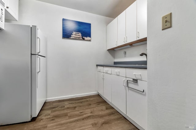 kitchen featuring white appliances, wood finished floors, white cabinetry, dark countertops, and baseboards