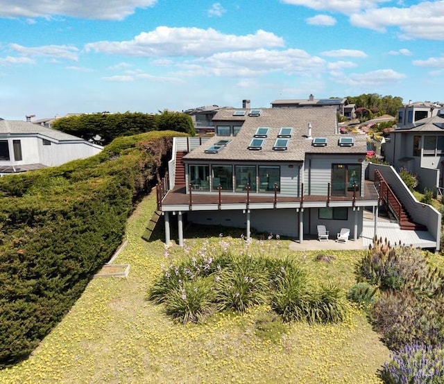 back of property with a patio area, stairs, roof with shingles, a wooden deck, and solar panels