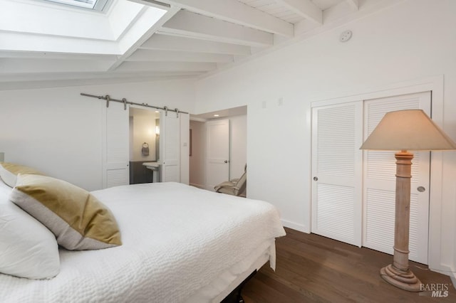 bedroom with wood finished floors, a skylight, baseboards, ensuite bathroom, and a barn door