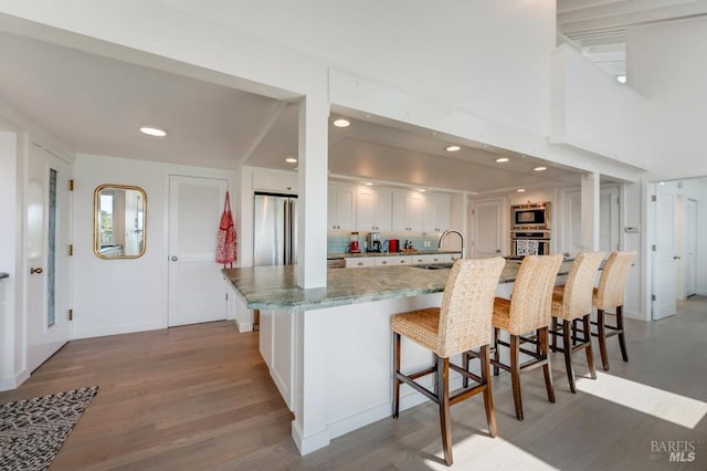 kitchen featuring stainless steel appliances, a sink, light wood-style flooring, a breakfast bar, and white cabinets