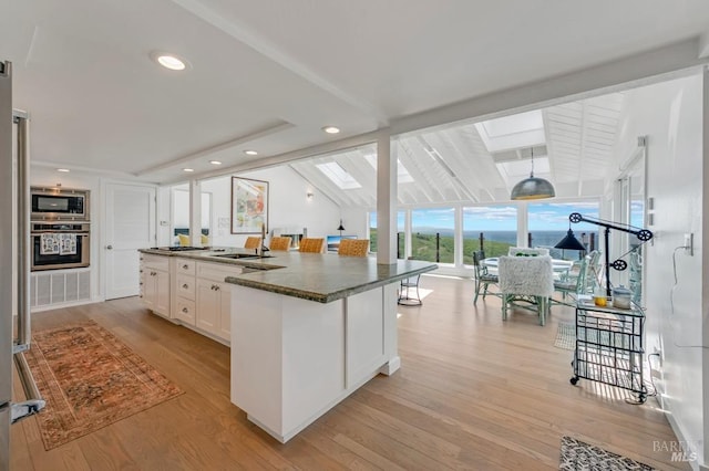 kitchen featuring appliances with stainless steel finishes, dark countertops, a skylight, a sink, and white cabinets