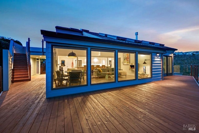 back of house at dusk featuring a deck and stairs