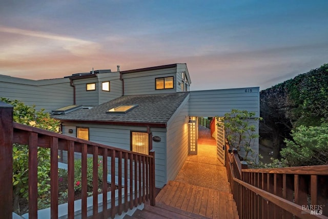 back of property at dusk featuring a shingled roof and a deck