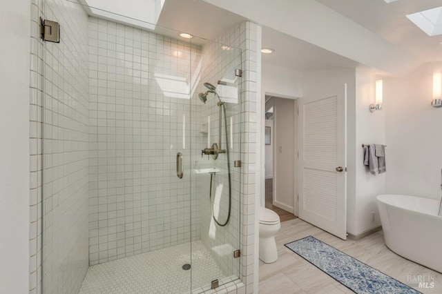 full bath featuring a skylight, a shower stall, toilet, and baseboards