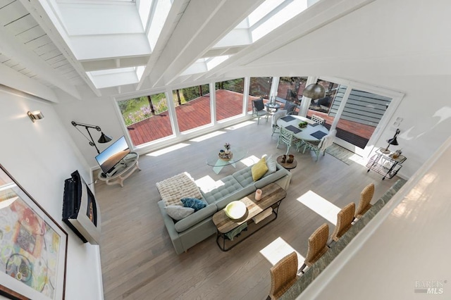 living room featuring a skylight, beamed ceiling, and wood finished floors