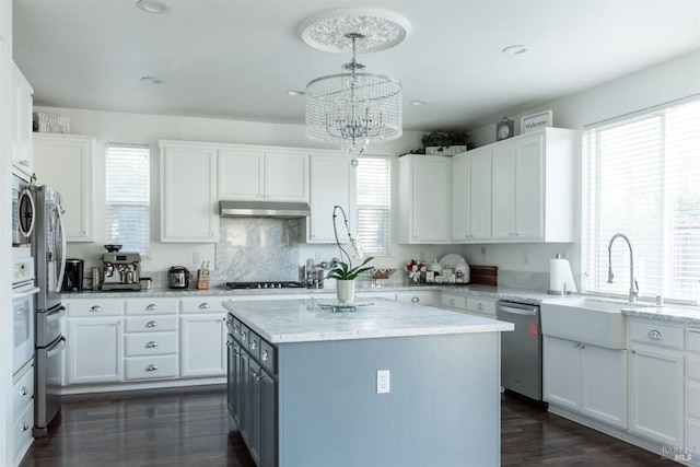 kitchen featuring stainless steel dishwasher, a sink, white cabinets, a kitchen island, and recessed lighting