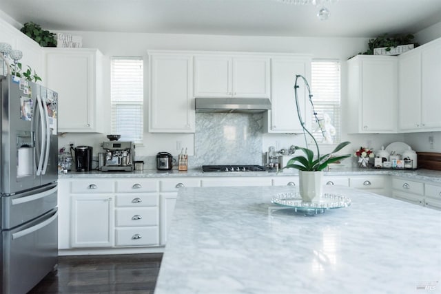 kitchen featuring stainless steel fridge with ice dispenser, under cabinet range hood, white cabinets, gas cooktop, and light stone counters